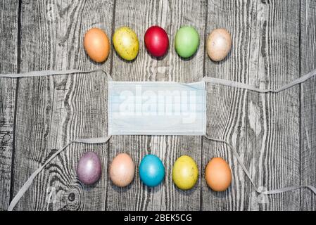 Three colored yellow easter eggs laying in medical mask on the wooden background. Coronavirus Covid-19. Concept photo. Easter 2020. Stock Photo