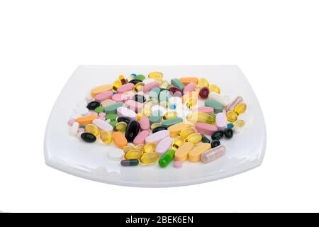 A pile of multi-colored pills on a white plate symbolizing food. Vitamins on a white isolated background. Different medicines. Tablets and pills of Stock Photo