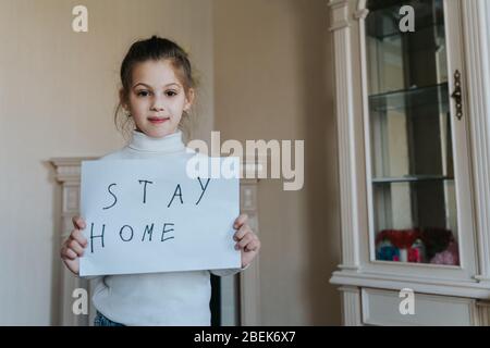 Stay at home concept. Small girl holding sign saying stay at home for virus protection and take care of their health from COVID-19. Stock Photo