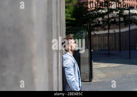 young bearded man leaning against wall and thinking Stock Photo