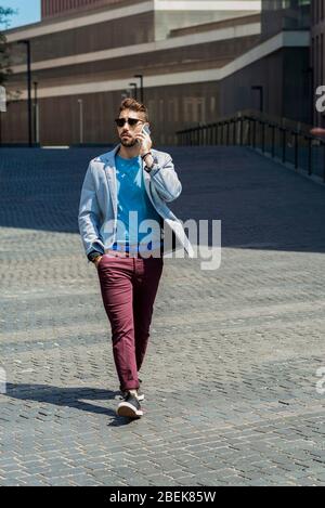 Portrait of cheerful modern businessman speaking by phone and smiling while walking outdoors Stock Photo