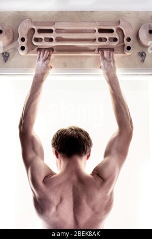 Climber's strong back and fingers in magnesia on the fingerboard. Back view. Man is doing a training on climbing fingerboard for rock climbing Stock Photo