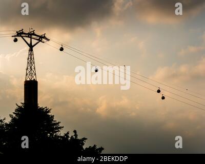 Cable cars between Singapore and Sentosa island silhouetted against dark ominous clouds. The cable cars are a symbol of Singapore tourism Stock Photo