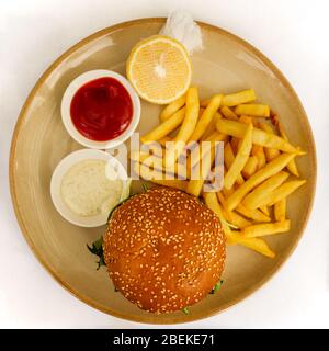 Flat lay of a burger and chips / French fries served with tomato ketchup, tartar sauce, and lemon on the side on white background Stock Photo