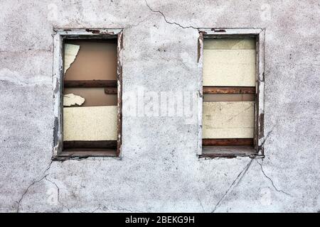 Boarded up windows and cracked peeled dirty walls of an abandoned old building. Stock Photo