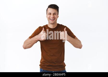 Portrait of cheerful, handsome satisfied caucasian man giving positive feedback, recommend product, thumbs-up pleased and look camera, like and Stock Photo