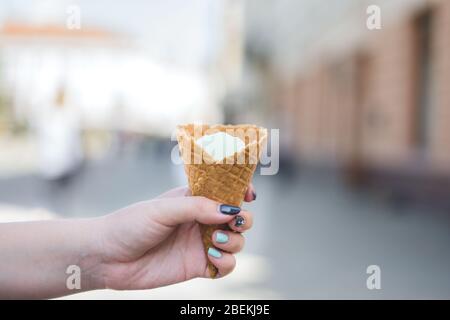 Girl's hand holds vanilla ice cream in waffle cone. Stock Photo
