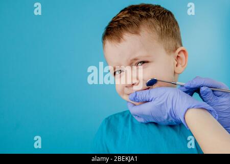 Small patient does not want to open the dentist's mouth on blue background. Dantist treats teeth. close up view of dentist treating teeth of little Stock Photo