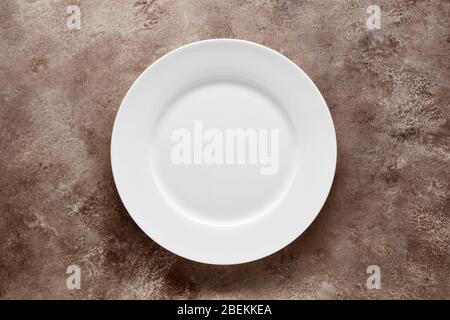 Empty white plate on brown textured background with copy space. Top view. Stock Photo