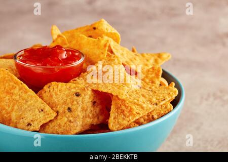 Mexican nachos or tortilla chips in a turquoise bowl with chili salsa dip sauce. Close up view. Stock Photo