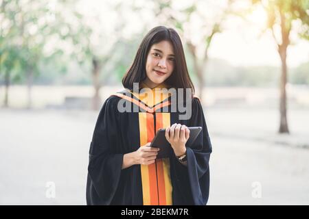 Young charming Asian female graduates celebrate her degree graduation after accomplishing a diploma certificate in commencement day. Stock Photo