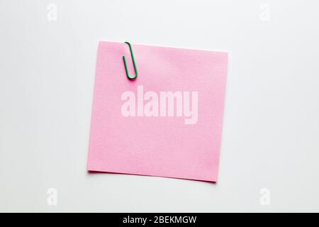 Blank pink note paper or notepad with a green paper clip on white background with copy space. Reminder text Stock Photo