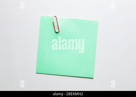 Blank green note paper or notepad with a red paper clip on white background with copy space. Reminder text Stock Photo