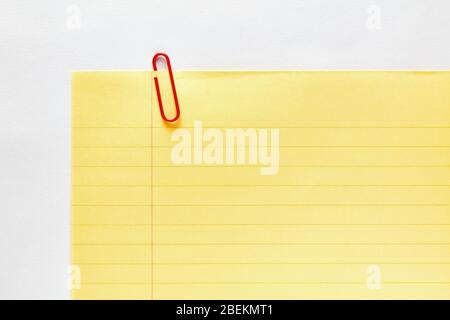 Red plastic paper clip attached to the corner of a blank yellow ruled or lined notebook paper. Close up view. Stock Photo