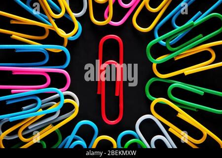 Red paper clip surrounded by colorful paper clips on black background. Stock Photo