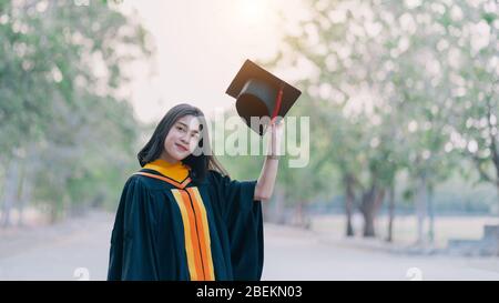 Young charming Asian female graduates celebrate her degree graduation after accomplishing a diploma certificate in commencement day. Stock Photo