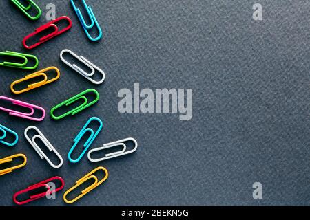 Colorful paper clips on black background with copy space. Flat lay macro view. Stock Photo