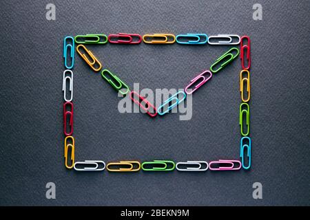 Colorful paper clips designed as envelope on black background. Concept of communication with letter or mail. Stock Photo