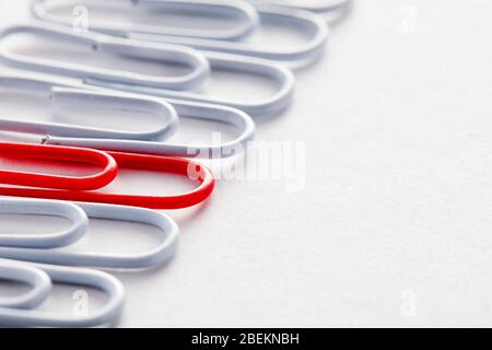 Red paper clip stands out from the crowd among white paper clips. Stock Photo