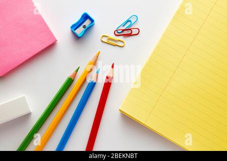 Stationery school supplies on white background. Colorful pencils, sharpener, eraser, notebook and paper clips. Stock Photo