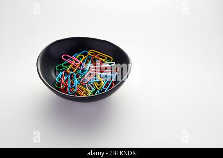 Heap of colorful paper clips in a black bowl on white background Stock Photo