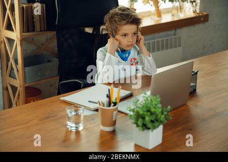 Caucasian teenboy as a doctor consulting for patient, giving recommendation, treating. Little doctor during cheking the lungs, listening. Concept of childhood, human emotions, health, medicine. Stock Photo