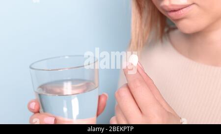 Close up of unhealthy young woman taking in pill and glass of water. Blue background. Stock Photo