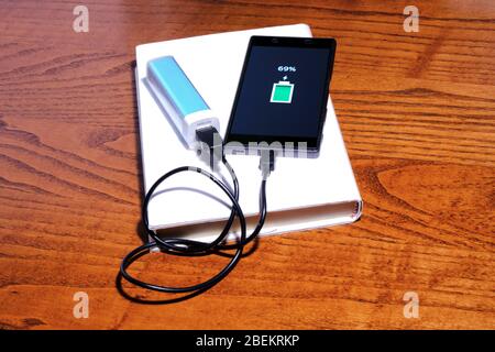 Smartphone in charge with a powerbank on  a book and destkop Stock Photo