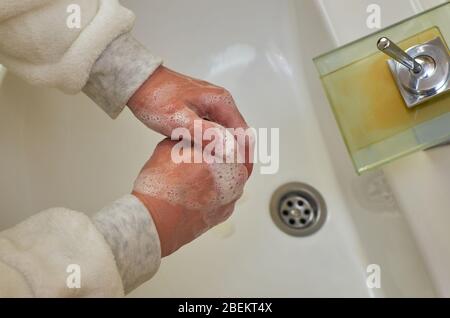 Foamy hands while washing over a sink in a bathroom Stock Photo