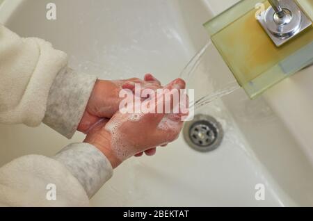 Foamy hands while washing over a sink in a bathroom Stock Photo