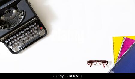 Retro black typewriter, glasses and notebooks of different colors on white background with with copy space for text. Stock Photo