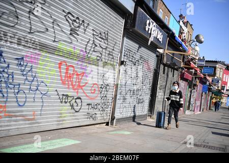 A man wearing a mask passes closed shops on Camden High Street, London, as the UK continues in lockdown to help curb the spread of the coronavirus. Stock Photo