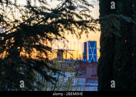 Madrid, Spain - March 23, 2020: Dramatic sunset on Madrid skyline financial district. Tree-framed view Stock Photo