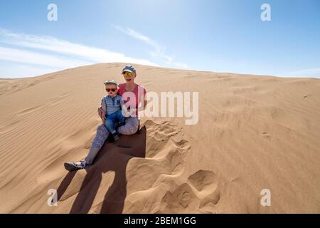 Mother and her 2 years old son enjoying sitting on Sahara sand dunes, Morocco, Africa Stock Photo