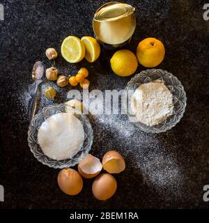 Various dessert ingredients including eggs, sugar, flour, gooseberries, lemons, a can on condense milk and a pinch of salt on a dark background Stock Photo