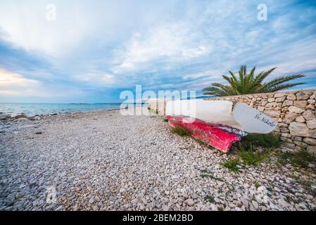 sunset on croatian stony beach with boat Stock Photo