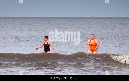 Portobello, Edinburgh, Scotland, UK. 14th April 2020. A hazy cloudy scene at the very quiet seaside due to the Coronavirus Lockdown, with mostly dog walkers and two female swimmers as part of their permitted excercise Emma and Ella enjoy a dip in the Firth of Forth. Stock Photo