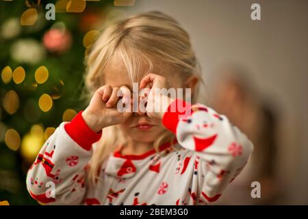 Sleepy young girl rubbing her eyes in front of a Christmas tree Stock Photo