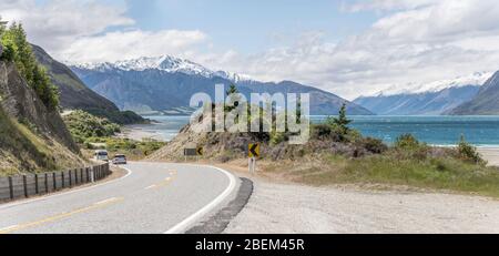 landscape of Hawea Alpine lake green eastern shore with road 6 on coast, shot in bright spring light from west coast near Albert Town, Otago, South Is Stock Photo