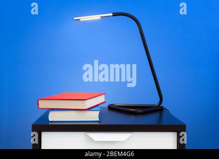 A modern lamp and two books on a nightstand against a blue colored interior wall Stock Photo