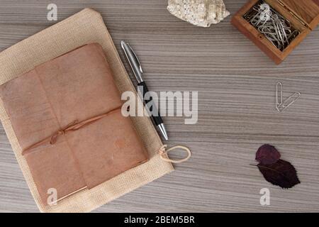 Top view of leather-bound book with pen and paperclips on wooden board Stock Photo