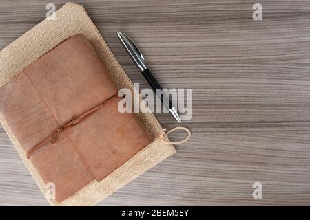 Top view of leather-bound book with pen on wooden board Stock Photo
