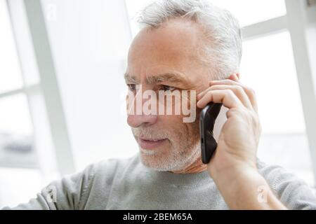 Photo closeup of serious mature man talking on cellphone while sitting in cafe indoors Stock Photo