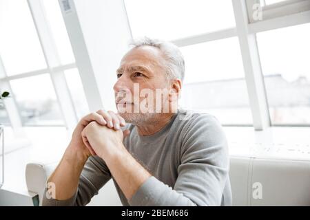 Image of a handsome serious mature senior businessman sit in cafe looking aside. Stock Photo