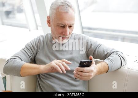 Photo of focused mature man in casual wear typing on cellphone while sitting in cafe indoors Stock Photo