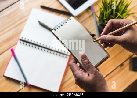 close up human holds blank notepad and pencils above wooden desk Stock Photo