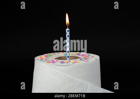 blue polka dot birthday candle in toilet paper roll with candy confetti sprinkles isolated on black Stock Photo