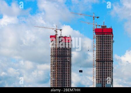 Two high-rise buildings and construction cranes on a background of blue sky with clouds Stock Photo