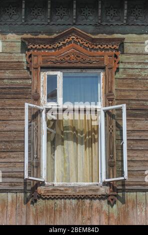 Open window in an old wooden house with carved platbands Stock Photo