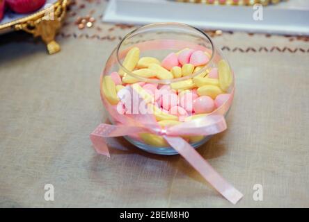 Pink and yellow candies in glass vase on white background . Multicolored round candy sweets in a round spherical vase aquarium Creative concept . Stock Photo